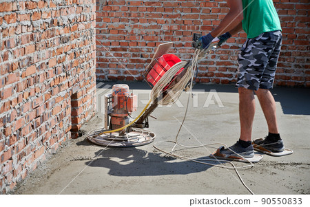 Close up of man builder using troweling machine while screeding floor. Worker finishing concrete surface with floor screed grinder machine at construction site on the top of residential building. Close up of man builder using troweling machine while screeding floor. Worker finishing concrete surface with floor screed grinder machine at construction site on the top of residential building. 90550833