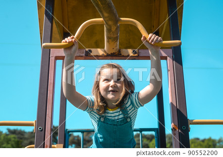 Happy six years old kid making sport outdoors. Little girl playing on playground, hanging walk along the monkey bars Happy six years old kid making sport outdoors. Little girl playing on playground, hanging walk along the monkey bars 90552200