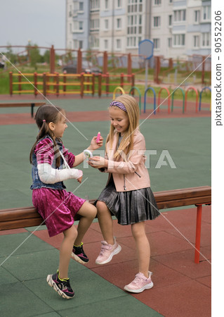 Funny humorous girls play beauty salon and paint each other's lips with lipstick. Babe with a cast on forearm holds lipstick in hand, her friend looks in the mirror. Children have lot of fun together Funny humorous girls play beauty salon and paint each other's lips with lipstick. Babe with a cast on forearm holds lipstick in hand, her friend looks in the mirror. Children have lot of fun together 90552206