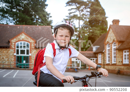 Happy smiling kid in helmet on bike. Child in protect helmet. Portrait of female primary school student wearing uniform with bicycle outside school buildings 90552208