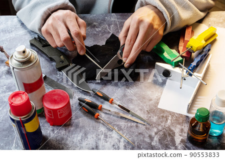 Sharpen the serrated knife. Sharpen a knife with a saw. Tool in hand. Oil, grindstones and tools on the table. Sharpen the serrated knife. Sharpen a knife with a saw. Tool in hand. Oil, grindstones and tools on the table. 90553833