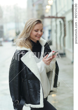 young blond slavic woman with cell phone in black leather jacket closeup street portrait young blond slavic woman with cell phone in black leather jacket closeup street portrait 90554190