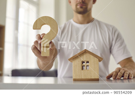 Confusion young man who is hesitant about buying his home shows wooden question mark. 90554209