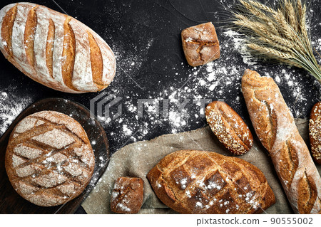 Top view of baguette, baked bread, flour and wheat spikes composition with wheat flour sprinkled around on a dark background 90555002