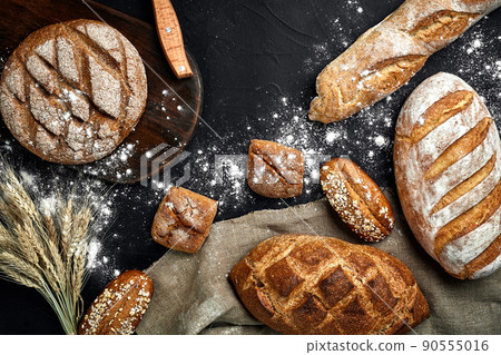 Homemade rye bread sprinkled with flour and various grains and seeds on a black background with spikelets of wheat or rye and oats. Homemade rye bread sprinkled with flour and various grains and seeds on a black background with spikelets of wheat or rye and oats. 90555016