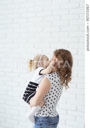 Mother holds her child with hearing aids and cochlear implants on white brick wall . Deaf and health concept 90555067