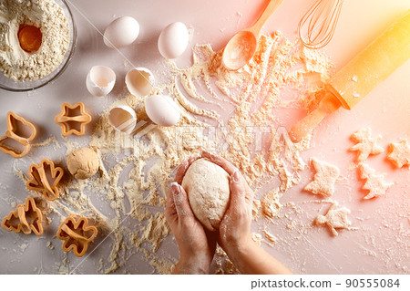 Female hands knead dough with egg and a rolling pin for preparation of cookies. Top view. Sun flare 90555084