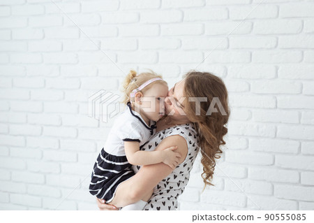 Mother holds her child with hearing aids and cochlear implants on white brick wall with copy space and place for advertising . Deaf and health concept 90555085