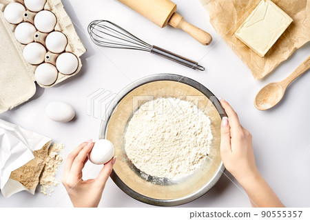 Making dough top view. Overhead of baker hands break egg on flour. Cooking ingredients for pastry on white table. Making dough top view. Overhead of baker hands break egg on flour. Cooking ingredients for pastry on white table. 90555357