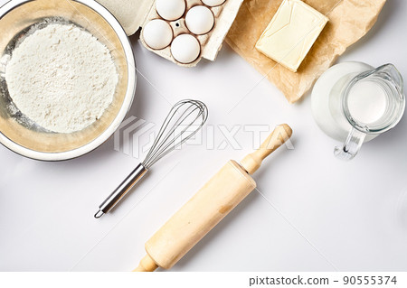 Preparation of the dough. A measurement of the amount of ingredients in the recipe. Ingredients for the dough: flour, eggs, rolling pin, whisk, milk, butter, cream. Top view, space for text 90555374