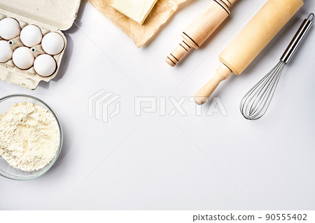 Preparation of the dough. A measurement of the amount of ingredients in the recipe. Ingredients for the dough: flour, eggs, rolling pin, whisk, butter. Top view, space for text Preparation of the dough. A measurement of the amount of ingredients in the recipe. Ingredients for the dough: flour, eggs, rolling pin, whisk, butter. Top view, space for text 90555402