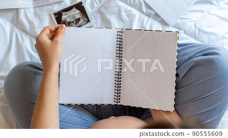 Baby list pregnant woman. Young pregnancy mother holding notepad. Pregnant lady writing check list of baby. Concept of maternity, expectation. Baby list pregnant woman. Young pregnancy mother holding notepad. Pregnant lady writing check list of baby. Concept of maternity, expectation. 90555609