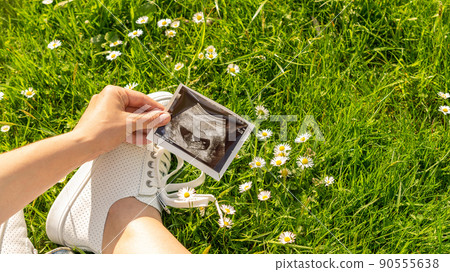 Ultrasound photo pregnancy baby. Woman holding ultrasound pregnant picture on grass flower background. Concept maternity, pregnancy, childbirth. Ultrasound photo pregnancy baby. Woman holding ultrasound pregnant picture on grass flower background. Concept maternity, pregnancy, childbirth. 90555638