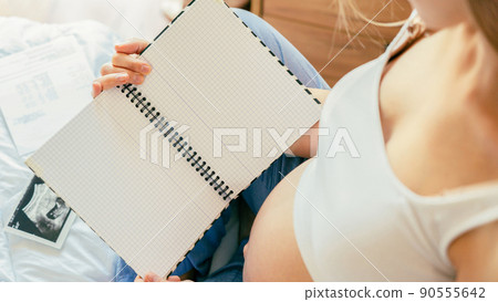 Baby list pregnant woman. Young pregnancy mother holding notepad. Pregnant lady writing check list of baby. Concept of maternity, expectation. Baby list pregnant woman. Young pregnancy mother holding notepad. Pregnant lady writing check list of baby. Concept of maternity, expectation. 90555642
