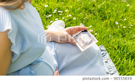 Ultrasound image pregnant baby photo. Woman holding ultrasound pregnancy picture on grass flower background. Pregnancy, medicine, pharmaceutics, health care and people concept. Ultrasound image pregnant baby photo. Woman holding ultrasound pregnancy picture on grass flower background. Pregnancy, medicine, pharmaceutics, health care and people concept. 90555659