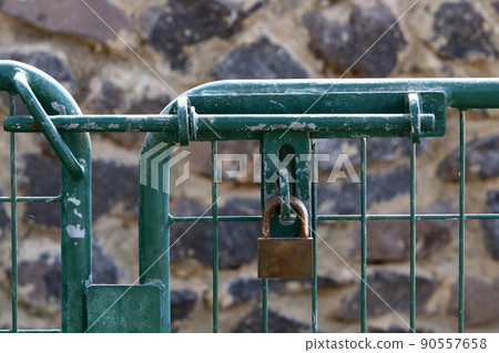 Padlock hangs on an iron closed gate with peeling paint and rust Padlock hangs on an iron closed gate with peeling paint and rust 90557658