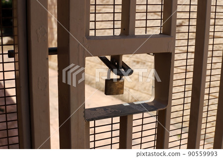Padlock hangs on an iron closed gate with peeling paint and rust 90559993