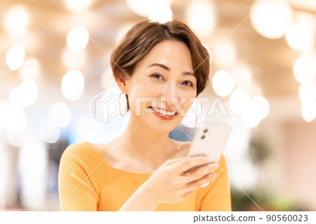 Middle-aged woman using a smartphone in glittering lighting Middle-aged woman using a smartphone in glittering lighting 90560023