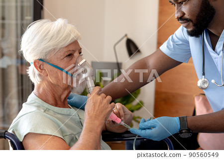 African american male health worker helping caucasian senior woman to use oxygen mask African american male health worker helping caucasian senior woman to use oxygen mask 90560549