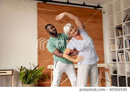African american male physiotherapist helping caucasian senior woman to perform stretching exercise 90560599