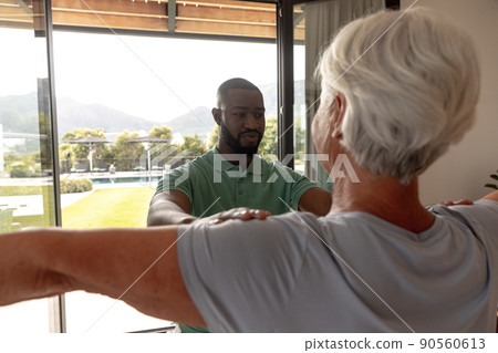 African american male physiotherapist helping caucasian senior woman to perform stretching exercise 90560613