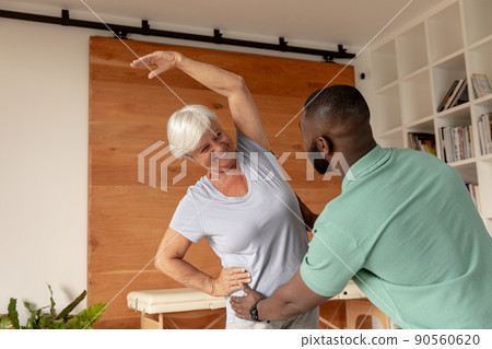 African american male physiotherapist helping caucasian senior woman to perform stretching exercise 90560620