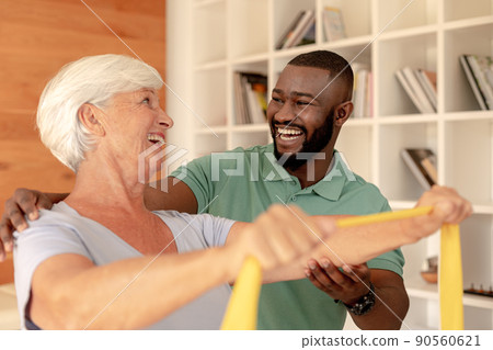 African american male physiotherapist helping senior woman to exercise with resistance bands 90560621