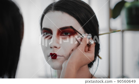 Close-up A young woman creates the image of a geisha for a girl. Makeup. Creating an image for an event Close-up A young woman creates the image of a geisha for a girl. Makeup. Creating an image for an event 90560649