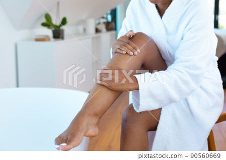 Mid section of woman in a bathrobe applying moisturizer on her leg sitting near bath tub Mid section of woman in a bathrobe applying moisturizer on her leg sitting near bath tub 90560669