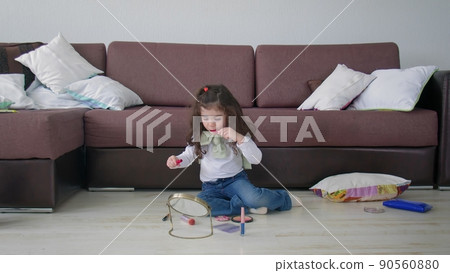 A little girl sits on the floor in a room and plays with makeup. Beauty and fashion 90560880