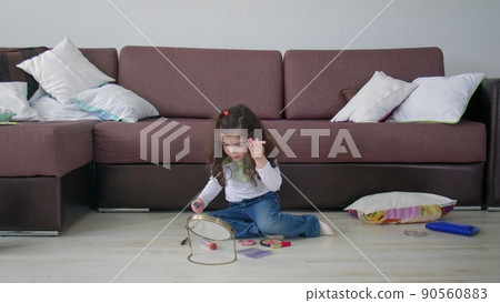 A little girl sits on the floor in a room and plays with makeup. Beauty and fashion 90560883