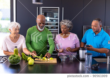 Multiracial senior friends making smoothie with granny smith apples and leaf vegetables in kitchen 90561009
