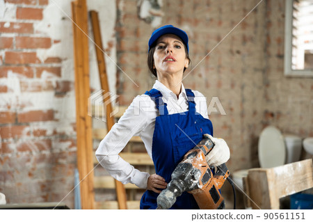 Workwoman standing at construction site with pneumatic chisel hammer 90561151