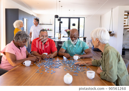 Multiracial senior friends solving jigsaw puzzle on wooden table while sitting in nursing home Multiracial senior friends solving jigsaw puzzle on wooden table while sitting in nursing home 90561268