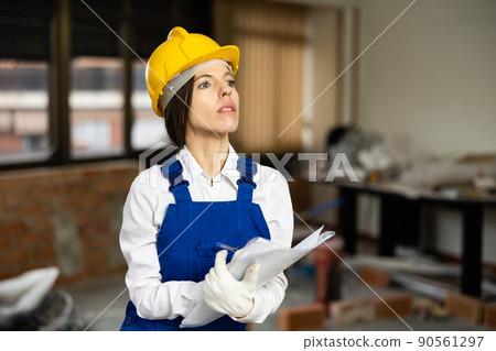 Positive female civil engineer taking notes while checking indoor construction site, satisfied with progress of work 90561297