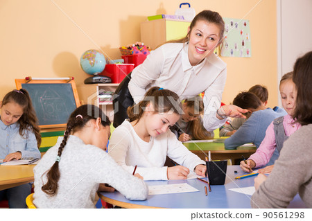 boys and girls sitting and teacher helping drawing 90561298