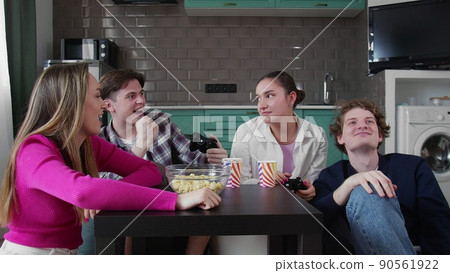Company of young cheerful friends sitting together chatting and playing console at house party. Fun with friends Company of young cheerful friends sitting together chatting and playing console at house party. Fun with friends 90561922