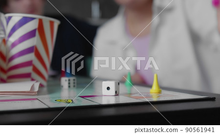 Close-up A group of friends are playing a board game with cards and dice. Girl's hand throws dice 90561941