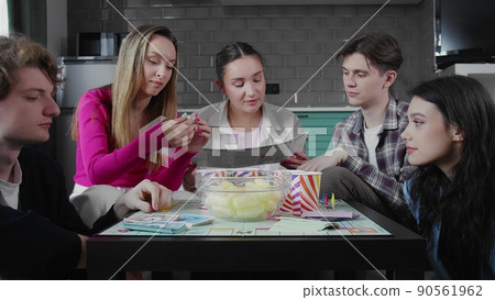 A group of friends playing a board game with cards and dice.. The girl reads the rules of the board game. A group of friends playing a board game with cards and dice.. The girl reads the rules of the board game. 90561962