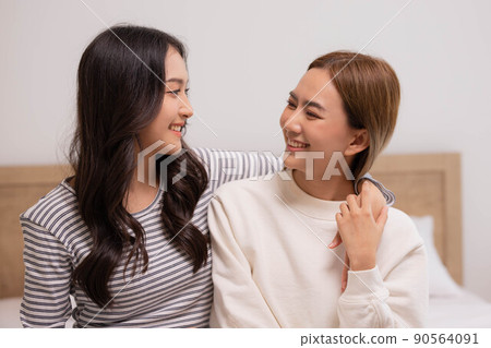 Happy LGBT lesbian couple lesbian embracing and looking together with love and romance on bed. 90564091