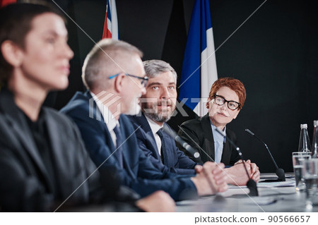 Young businesswoman in eyeglasses talking to her international colleagues at table before starting the conference 90566657
