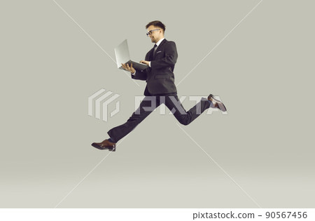Successful young businessman who is in hurry to do lot of work working on laptop on run. 90567456