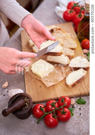Woman spreading tasty organic butter onto bread over grey table with wooden cutting board 90570106