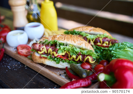 BBQ hot dog served with vegetables and French fries and sauces on wooden serving board 90570174