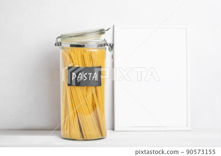 Organization of storage in the kitchen. Pasta in glass container on a kitchen table. White empty frame for text. Zero waste storage Organization of storage in the kitchen. Pasta in glass container on a kitchen table. White empty frame for text. Zero waste storage 90573155