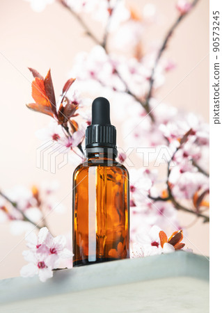 Amber glass dropper bottle and spring cherry blossom flower on marble shelf. Skincare products , natural cosmetic. Beauty concept for face and body care, ow angle view, 90573245