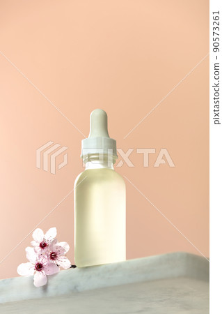 White glass dropper bottle with white lid on white marble shelf, natural spring background. 90573261