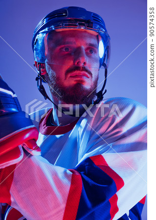 Closeup portrait of professional hockey player in sports uniform and protective equipment isolated on purple background in neon. Concept of sport, healthy lifestyle, hobby, movement, action. Closeup portrait of professional hockey player in sports uniform and protective equipment isolated on purple background in neon. Concept of sport, healthy lifestyle, hobby, movement, action. 90574358