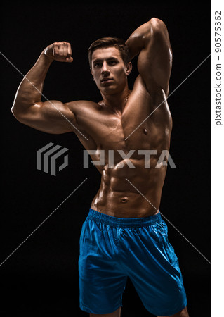 Muscular and fit young bodybuilder fitness male model posing over black background. Muscular and fit young bodybuilder fitness male model posing over black background. 90575362