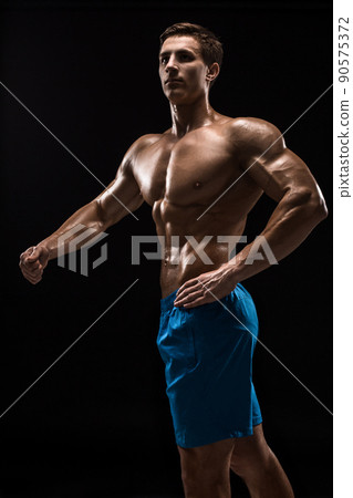 Muscular and fit young bodybuilder fitness male model posing over black background. Muscular and fit young bodybuilder fitness male model posing over black background. 90575372